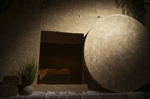The open tomb, its round stone rolled aside, lit by one warm light.